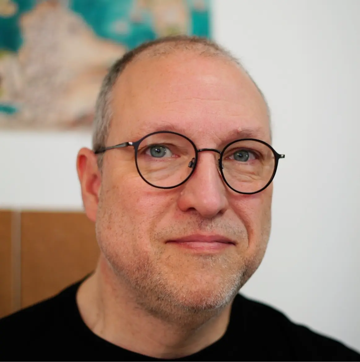 Headshot of a balding man with round glasses and stubble.